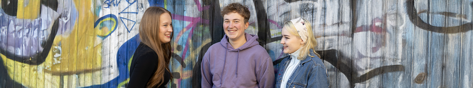 kolme nuorta ihmistä graffitiseinän edessä.