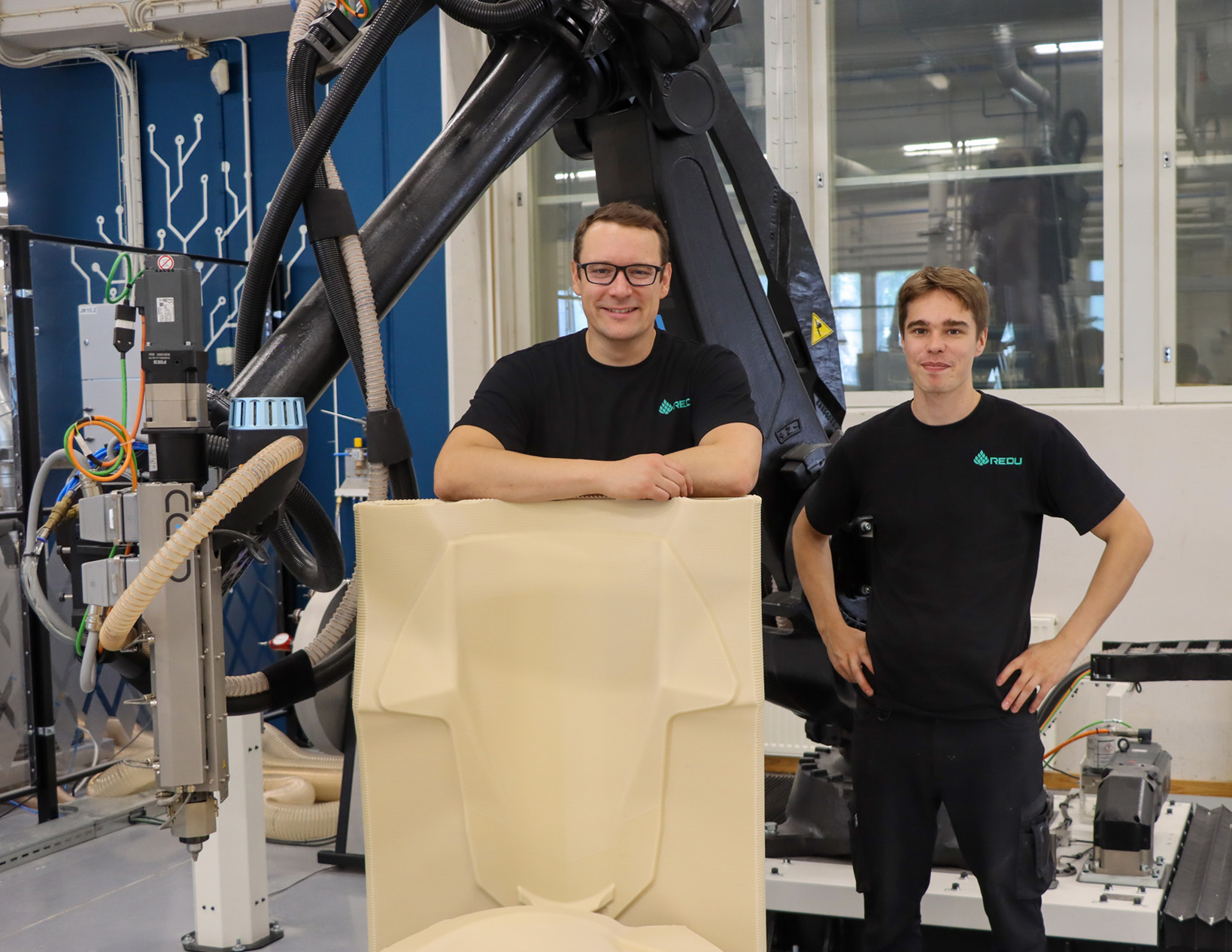 Kaksi henkilöä pitää robottisolun tekemän suurmuotin kanssa