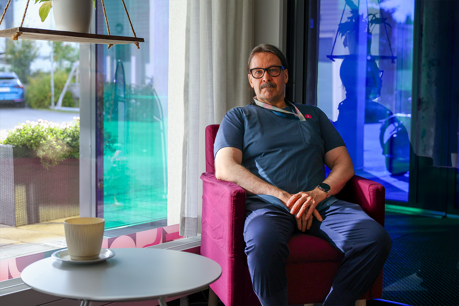 Markku Miettunen istumassa punaisella nojatuolilla ikkunan edessä